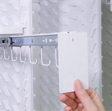 A person placing a white card on a wall with multiple hooks.